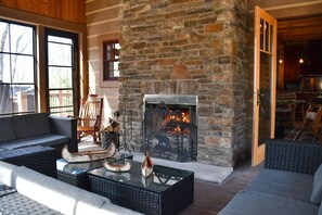 Ein Kamin aus Stein mit Feuer, ein Sofa und ein Couchtisch in einem Raum mit Holzwänden und großen Fenstern.