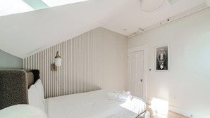 Ein Schlafzimmer mit einem Bett, einer Wandleuchte, einer Tür und einem gerahmten Bild.