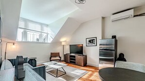 Ein modernes Wohnzimmer mit schrägen Wänden, einem Flachbildfernseher, einem Kühlschrank und einem Esstisch.