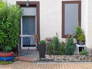 A patio with a table and chairs, surrounded by potted plants and a stone wall.