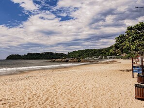 A beach with a sandy shore, a rocky outcrop, and a signboard. - Casa Para 12 em Itaja Piscina e Churrasqueira (Itajai)
