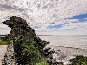 A coastal landscape with a prominent rock formation, a stone wall, and a view of the sea. - Casa Para 12 em Itaja Piscina e Churrasqueira (Itajai)