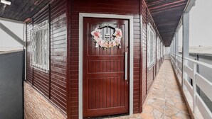 Käytävä, jossa on puinen ovi, kivilaatoitettu lattia ja oikealla puolella metallinen kaide.