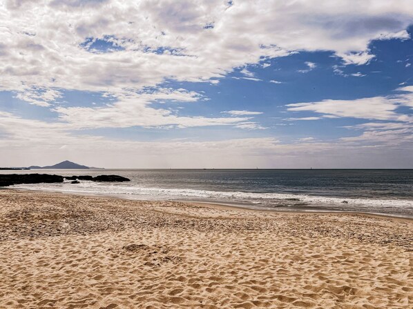 A beach with sand, water, and a distant mountain.