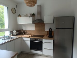 Eine moderne Küche mit weißen Schränken, einem Edelstahl-Kühlschrank, einem eingebauten Backofen, einer Spüle und einem Fenster, das für natürliches Licht sorgt.