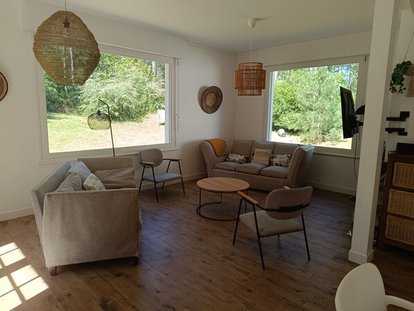 Ein geräumiges Wohnzimmer mit einer Couch, Sesseln, einem Couchtisch und großen Fenstern mit Blick auf Grünflächen.