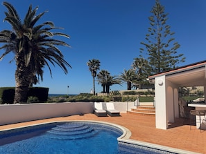 A swimming pool with lounge chairs, a patio area, and a view of the sea. - Charming 4-bedroom villa with Full Ocean View in Carvoeiro perfect for families (Carvoeiro)