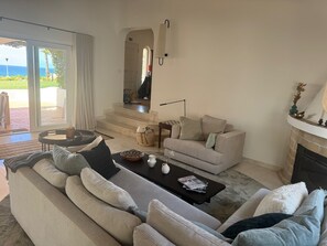 A living room with a sofa, a coffee table, and a fireplace. There is a view of the outdoors through a glass door. - Charming 4-bedroom villa with Full Ocean View in Carvoeiro perfect for families (Carvoeiro)