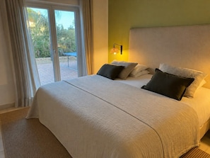 A hotel room with a large bed, a view through the glass door, and a wall-mounted lamp. - Charming 4-bedroom villa with Full Ocean View in Carvoeiro perfect for families (Carvoeiro)