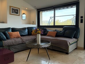 Ein modernes Wohnzimmer mit einem Ecksofa, einem runden Couchtisch und einem großen Fenster mit Blick ins Freie.