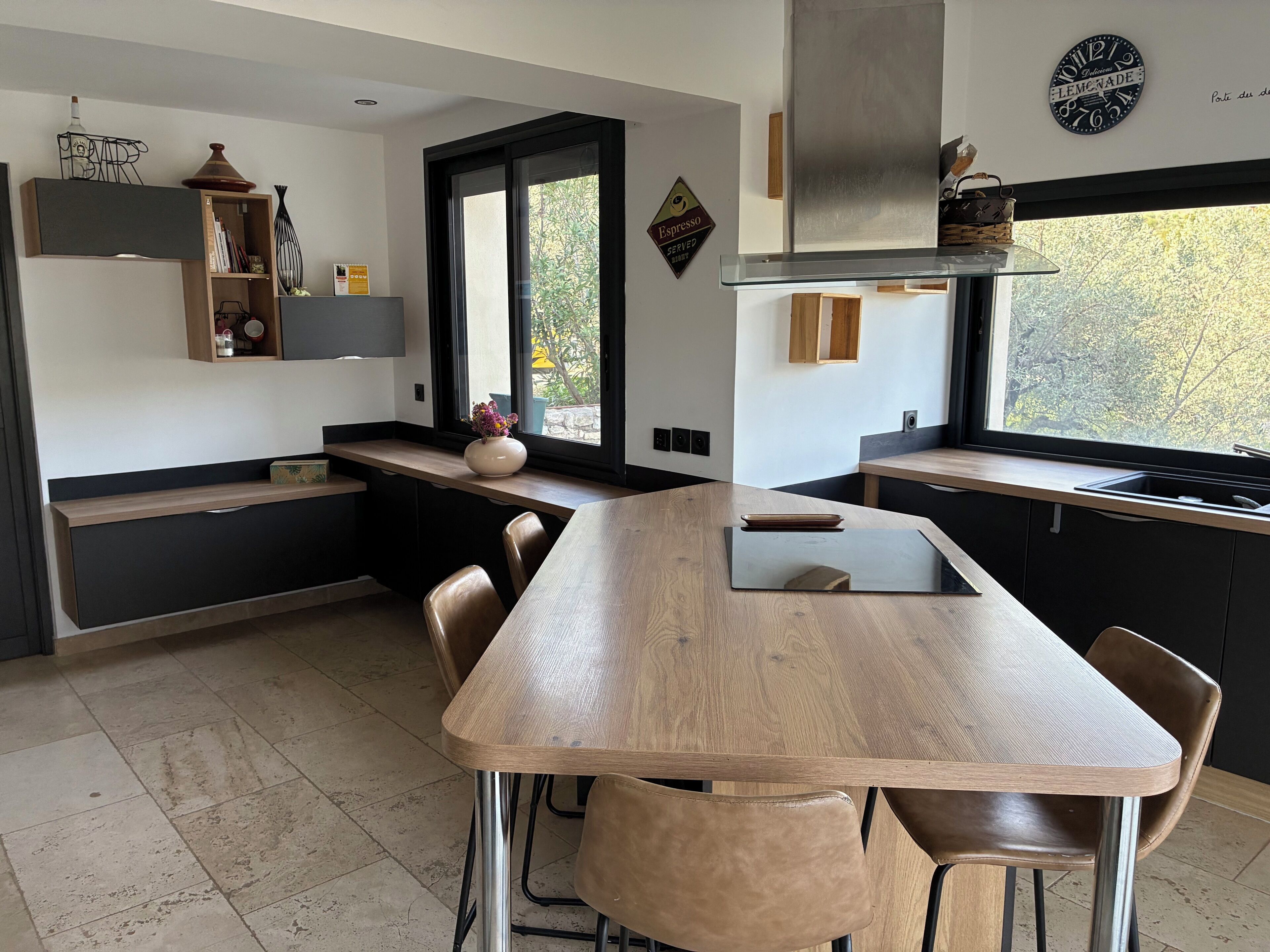Een moderne keuken met een houten eiland, zwarte kasten en een raam met uitzicht op bomen.
