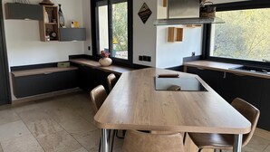 Una cocina moderna con isla de madera, armarios negros y ventana con vistas a árboles.