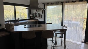 Cocina moderna con una isla grande, taburetes de bar, una ventana con vistas a árboles y una tetera de acero inoxidable.
