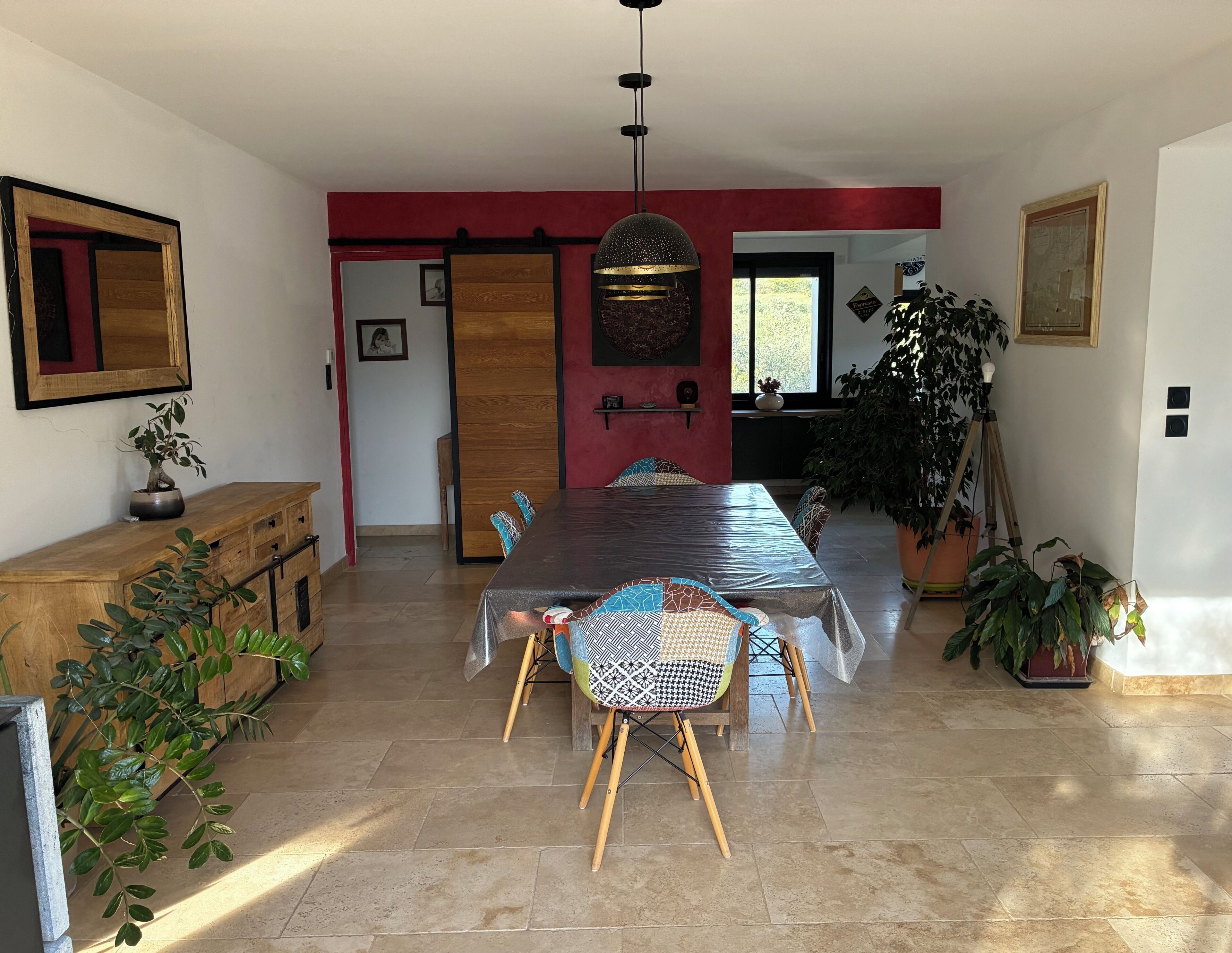 A dining area with a long table, chairs, and potted plants.