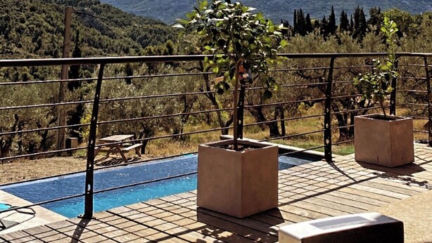 Zona de piscina con vista a montañas, rodeada por una terraza de madera y baranda metálica.