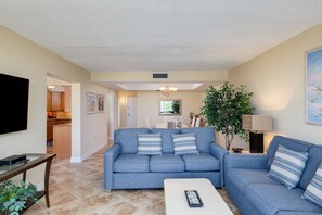 Ein Wohnzimmer mit einer Couch, einem Couchtisch, einem Fernseher und einer Küche im Hintergrund.