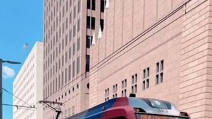 Un train rouge et blanc est garé dans une gare, avec un bâtiment en briques en arrière-plan.