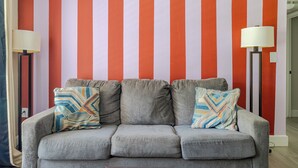 Un canapé gris agrémenté de coussins à motifs, placé contre un mur à rayures verticales.