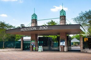 Der Eingang zum Houston Zoo mit Schild, Tor, Mülleimern und Zaun.