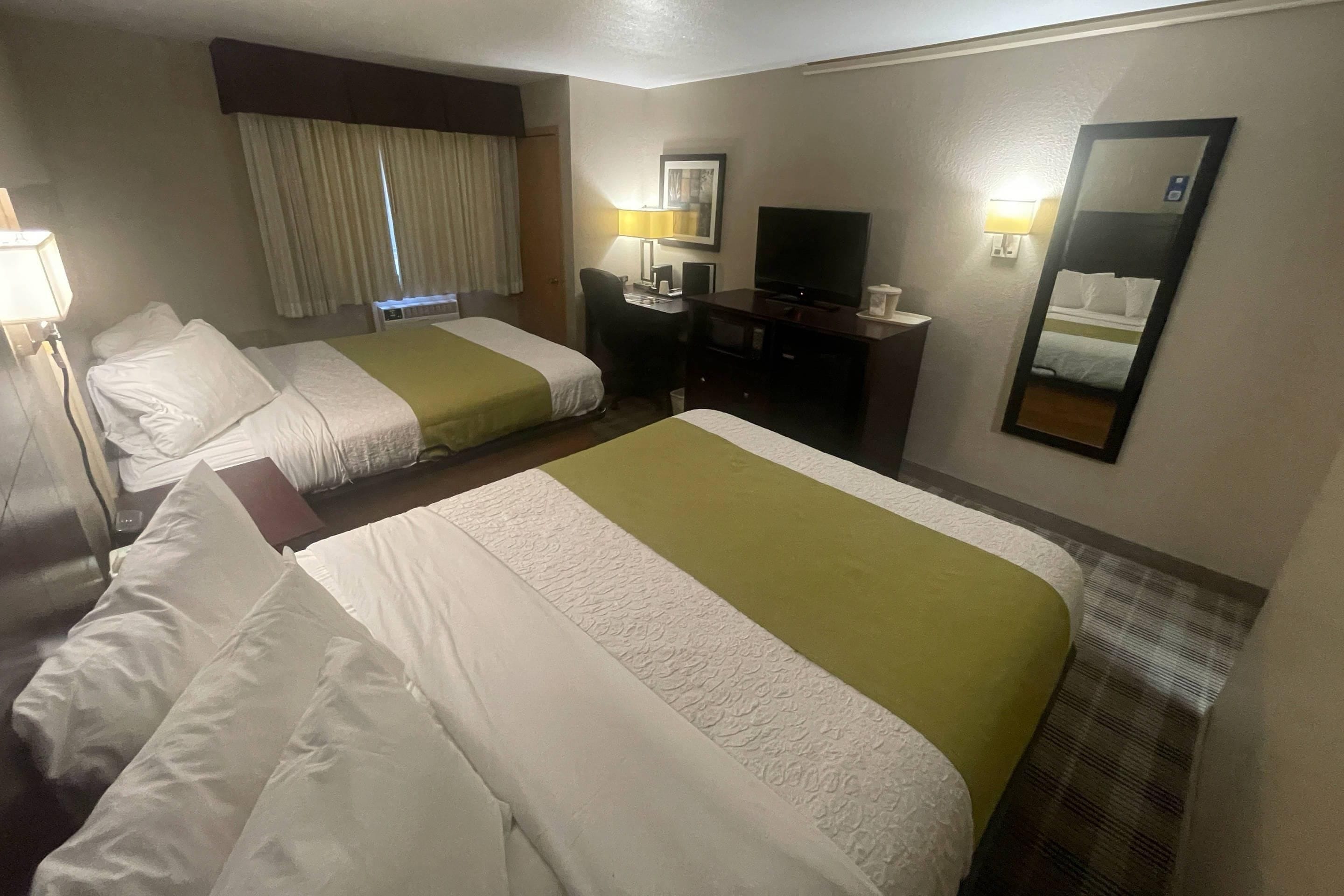 Una habitación de hotel con dos camas, un escritorio, un televisor y un espejo.