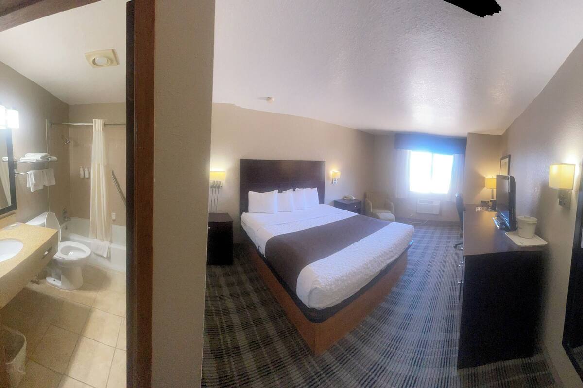 Habitación de hotel con cama, mesita de noche, espejo y vista al baño.