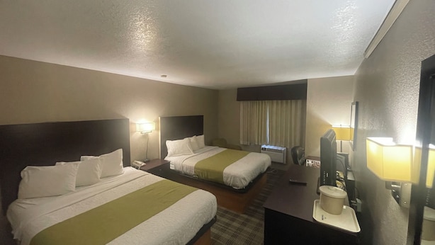 A hotel room with two beds, a desk, a chair, a TV, and a window with curtains.