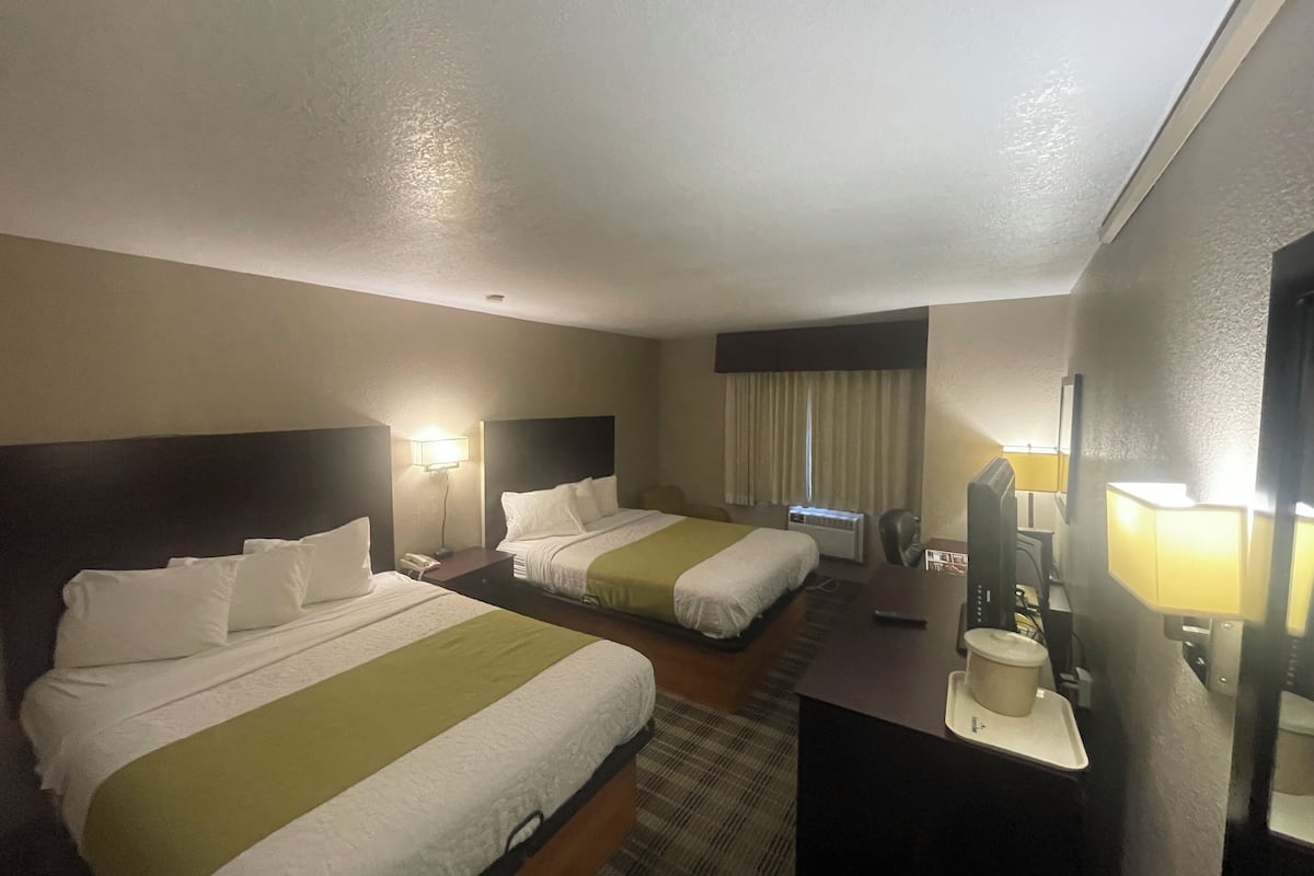 Habitación de hotel con dos camas, un escritorio, una silla, un televisor y una ventana con cortinas.