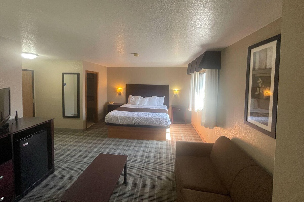 A hotel room with a bed, bedside tables, a desk, a chair, and a television.