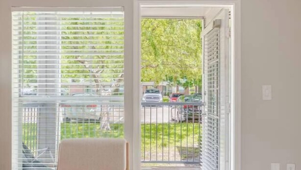 A room with a chair, a round table, and a view through a door to an outdoor area with a railing. - Fruity King 1BR facing NRG |near Med Center | Pool (Houston)