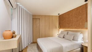 A modern bedroom with a large bed, a bedside table, a nightstand, a wall-mounted light, and a wooden panel wall. - Casa do Livro - E a de Queir s Apartment by Minho (Guimarães)