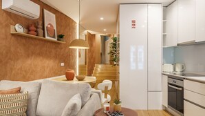 A modern kitchen with white cabinets, a built-in oven, and a dining area with a sofa and table. - Casa do Livro - E a de Queir s Apartment by Minho (Guimarães)