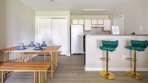 A modern kitchen with white cabinets, a central island with bar stools, and a dining area with a wooden table and blue bowls. - King Queen 2BR /walk to NRG /1mi to MD Anderson (Houston)