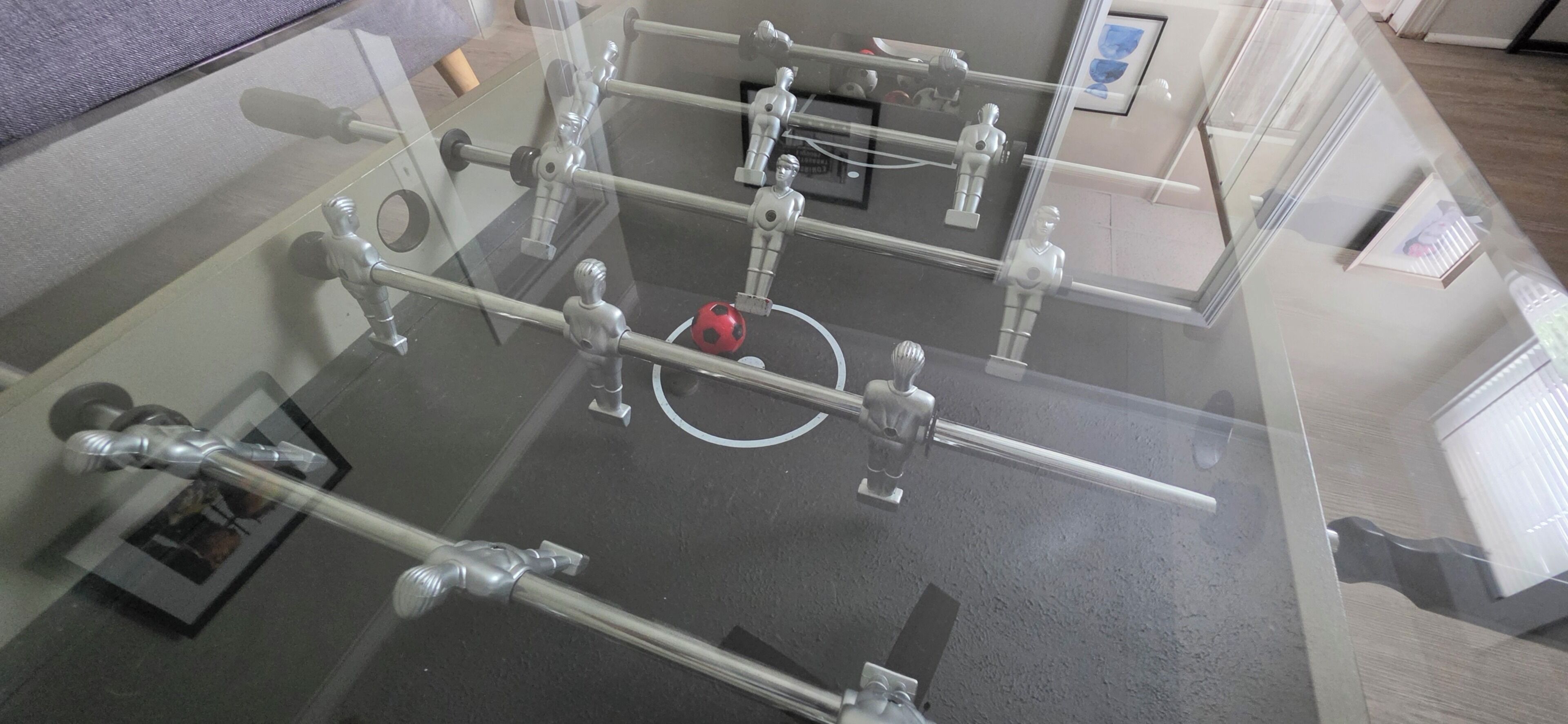 A tabletop foosball table with a red ball in play, surrounded by metallic figures.