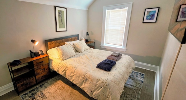 A bedroom with a bed, bedside tables, a lamp, a window, and artwork on the walls.