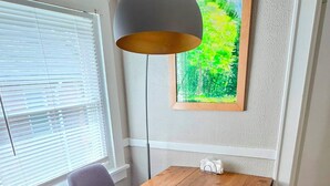 A dining area with a wooden table, grey upholstered chairs, a pendant lamp, a framed painting, and a white wall.