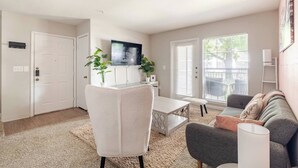 A living room with a sofa, a coffee table, a TV, and two potted plants. - Paris 1BR /5 min walk to NRG /By Medical Center (Houston)