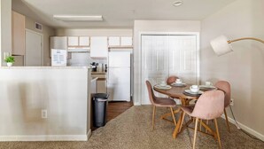 A compact kitchen with a refrigerator, a dining table with chairs, a trash bin, and a lamp. - Paris 1BR /5 min walk to NRG /By Medical Center (Houston)