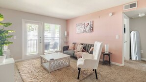 A living room with a sofa, a coffee table, a chair, a plant, and a painting on the wall. - Paris 1BR /5 min walk to NRG /By Medical Center (Houston)
