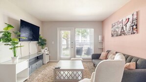 A modern living room with a flat-screen TV, a sofa, a coffee table, and a potted plant. - Paris 1BR /5 min walk to NRG /By Medical Center (Houston)