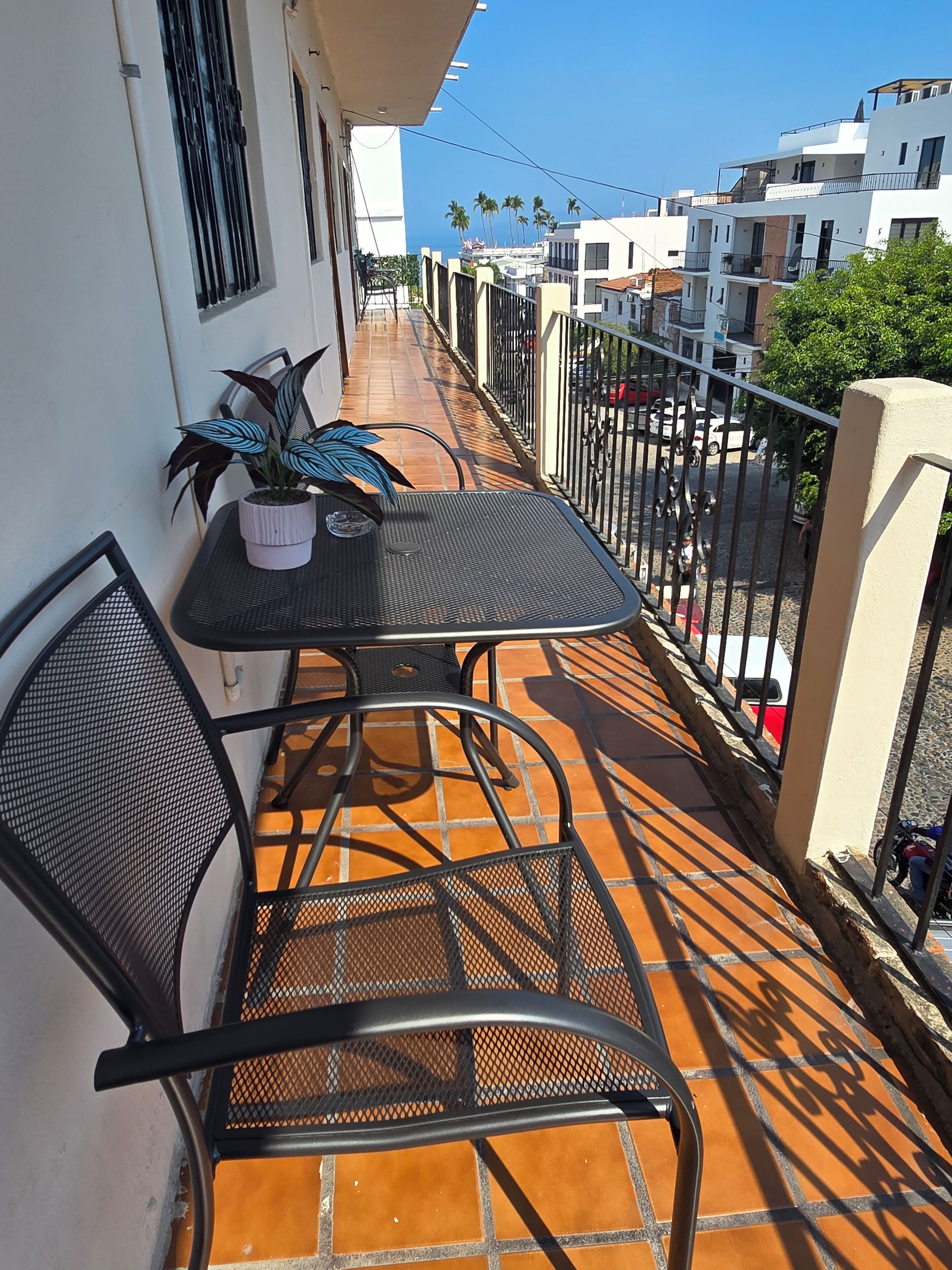 Un balcon avec une table et des chaises, un pot de fleurs et une vue sur la rue et les immeubles.