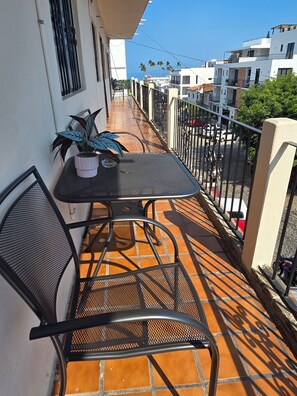 Un balcon avec une table et des chaises, un pot de fleurs et une vue sur la rue et les immeubles.