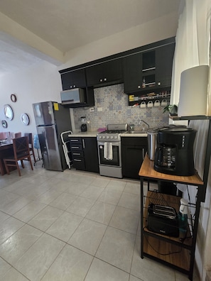 A kitchen with black cabinets, a stainless steel refrigerator, a gas stove, and a coffee maker. - COLIBRI APARTMENT FOR 4 PEOPLE, VERY CLOSE TO THE MALECÓN, BARS, AND RESTAURANTS (Puerto Vallarta)