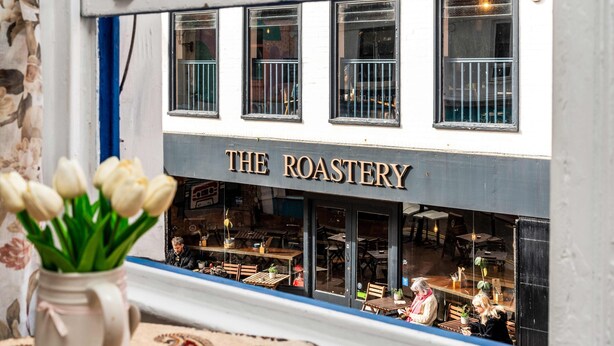 Een restaurant genaamd 'The Roastery' met zichtbare buitenterras door de ramen.