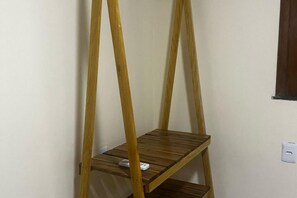 A wooden shelf unit with two levels, a white electrical outlet, and a window with a dark frame.