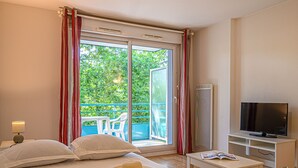 A hotel room with a bed, a television, a small table, and a view of greenery through the window. - Près de la plage et du centre | Piscine sur place (PLESCOP)
