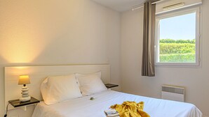Hotelkamer met een bed, een bedlampje, een raam met gordijnen en een wandairconditioner.