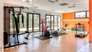 A gym with cardio machines, weightlifting equipment, and a large window offering a view of the outdoors.