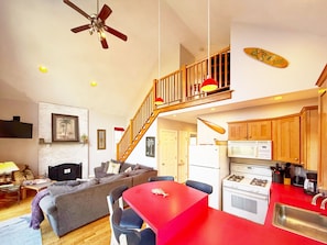 A living room with a sofa, a red table, and a kitchen with wooden cabinets and a stove.