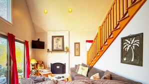Una sala de estar con un sofá, una chimenea, una escalera y una ventana con cortinas.