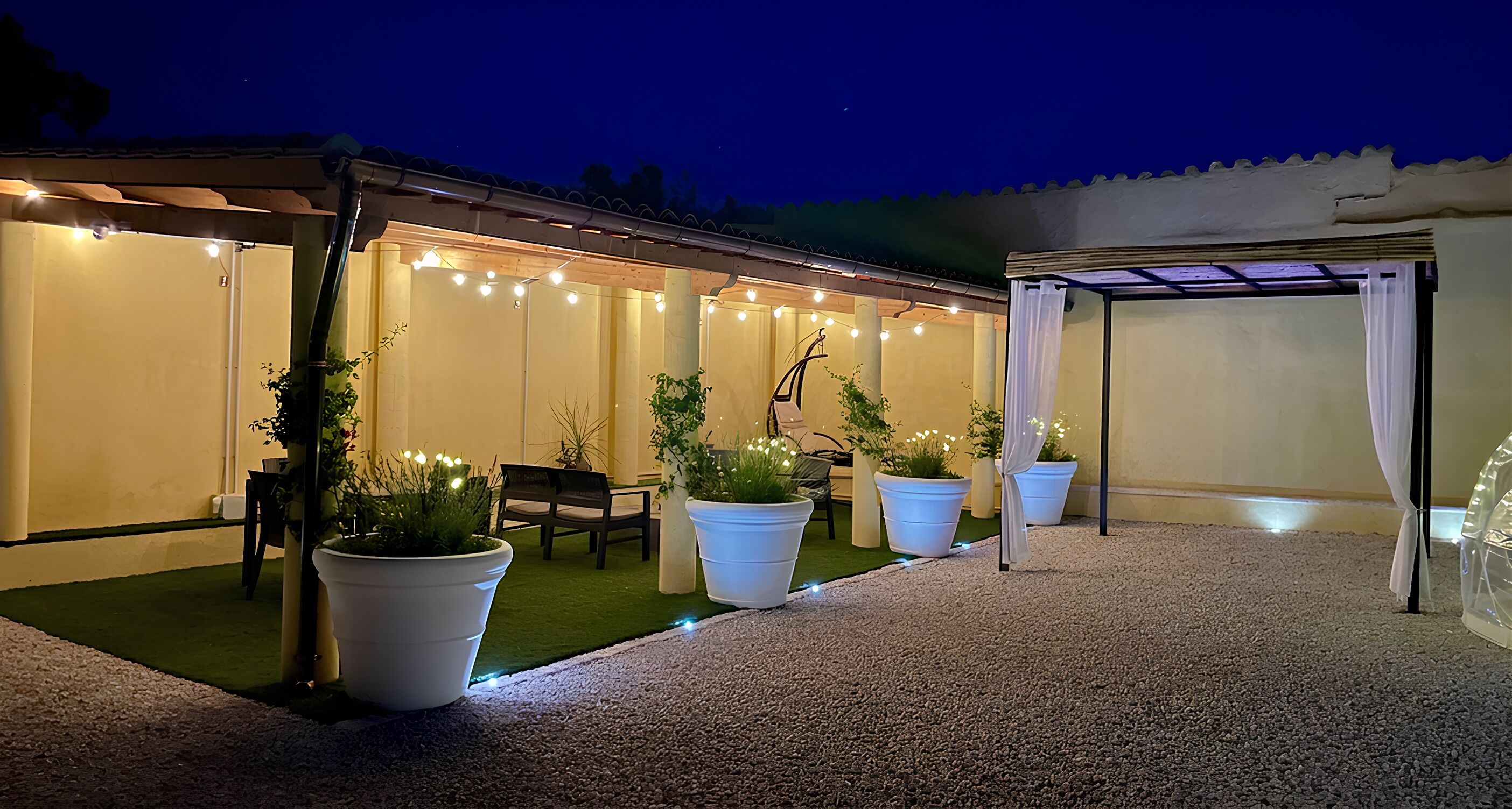 Un espacio al aire libre con macetas, un banco de madera y luces colgantes.